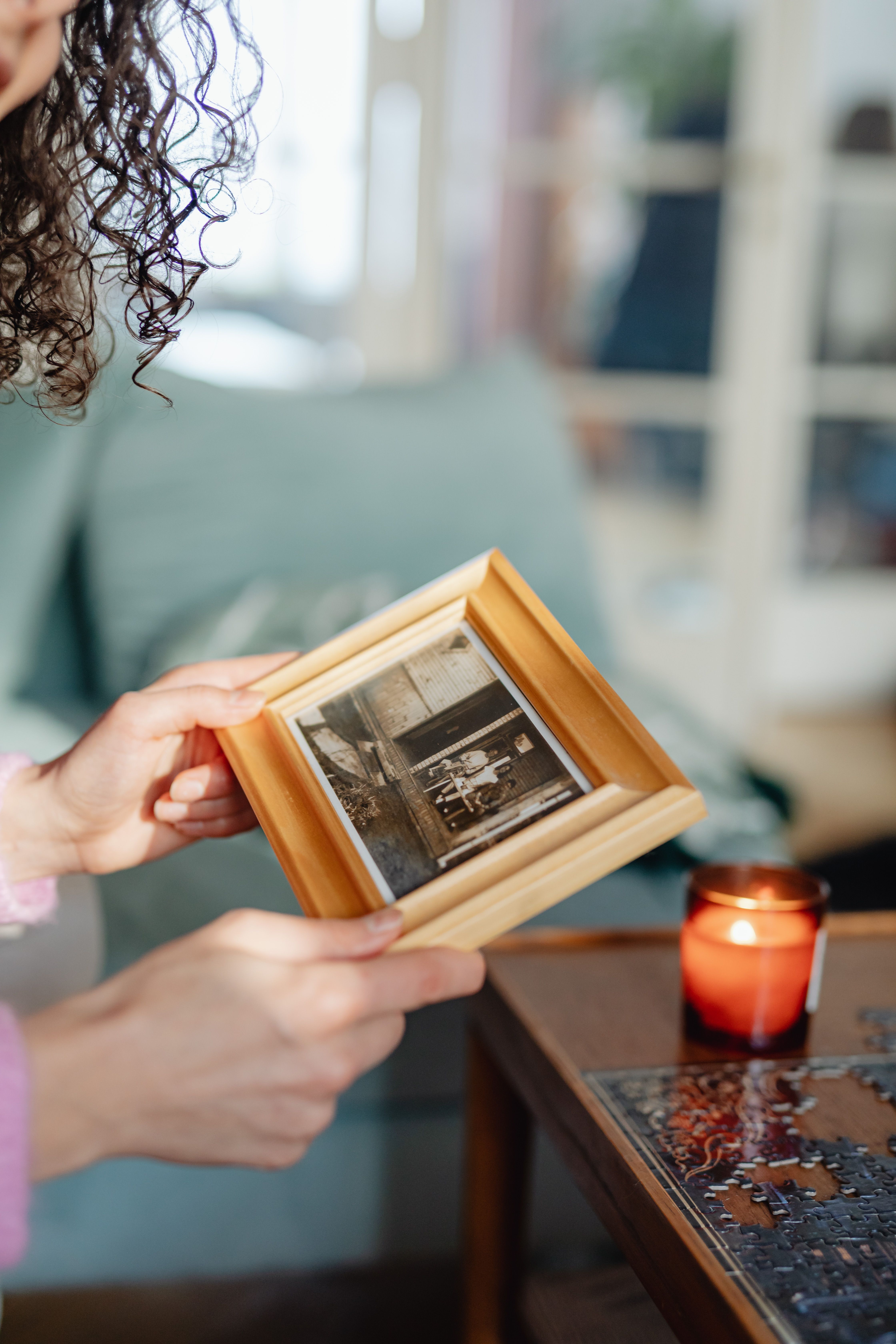 A person holds a framed family photograph beside a candle in a quiet home.
